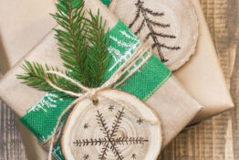 Christmas gift box in rustic style wrapped in craft paper with decor of wooden sliced with woodburning symbol.