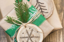Christmas gift box in rustic style wrapped in craft paper with decor of wooden sliced with woodburning symbol.